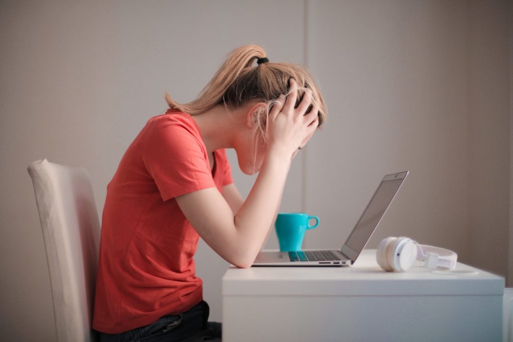 young woman holding her head in front of laptop due to stress