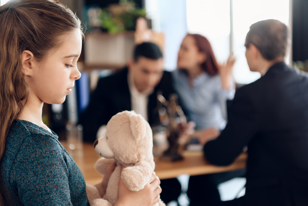 child holding her teddy bear while her parents are arguing in front of the lawyer